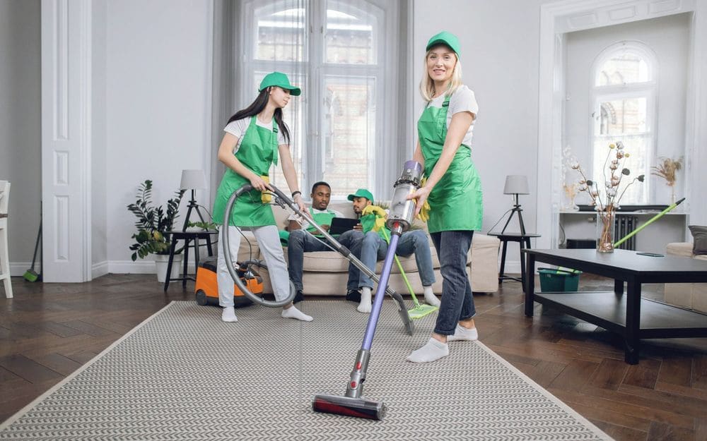 Två städare i gröna förkläden dammsuger ett ljust rum